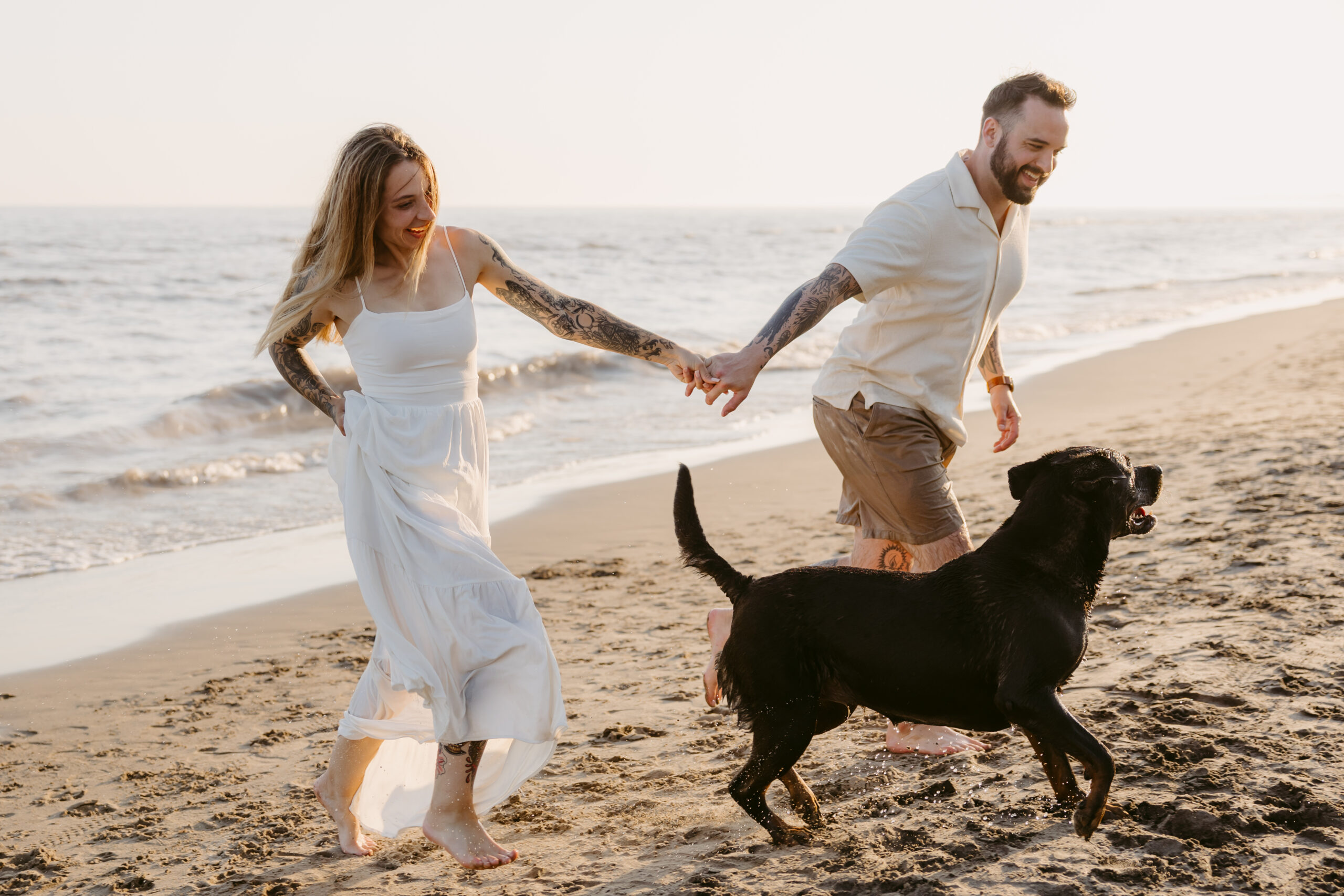 Couple running barefoot across Long Point Beach at sunset with their dog.