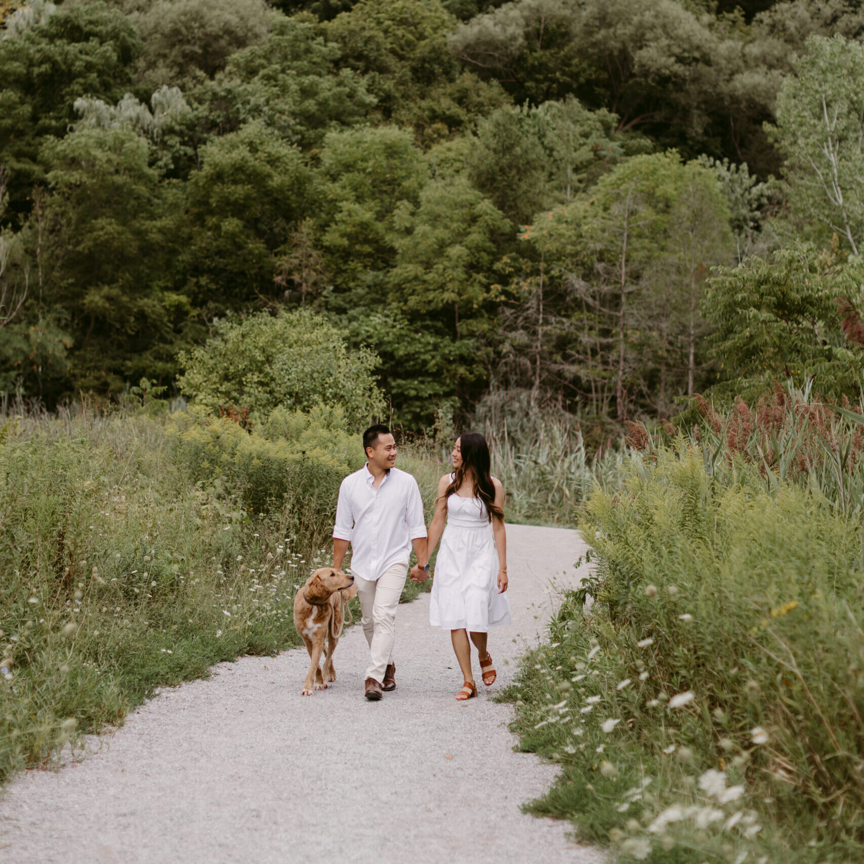 Couple dressed in white walking along the path in a summer field.