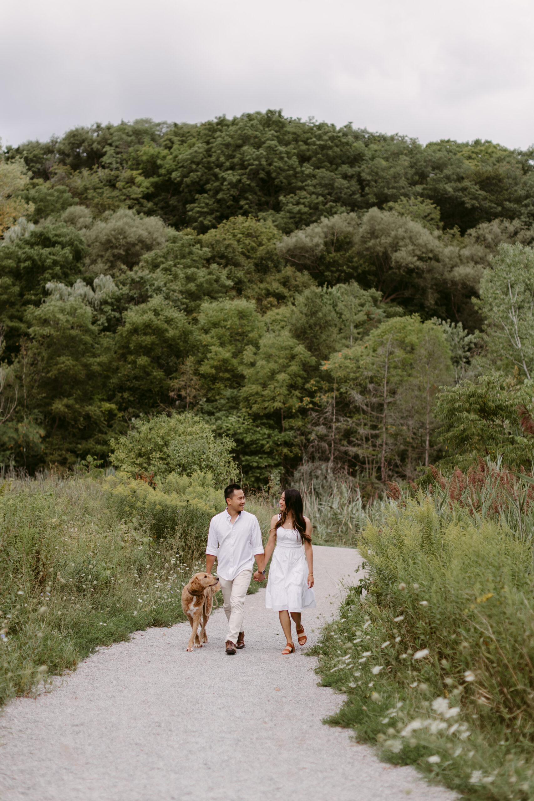 Couple dressed in white walking along the path in a summer field.