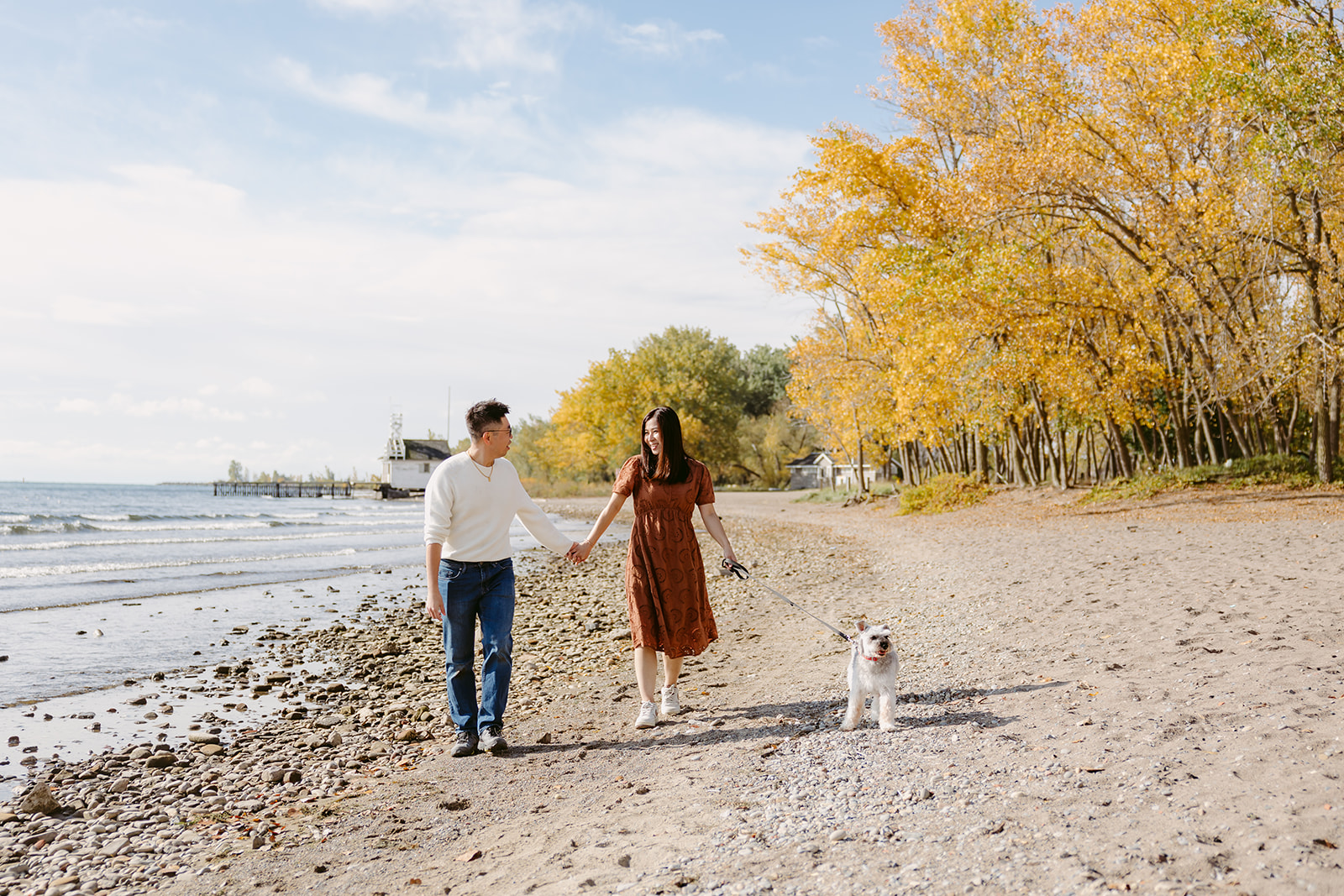 A couple walking with fall leaves along the beach.
