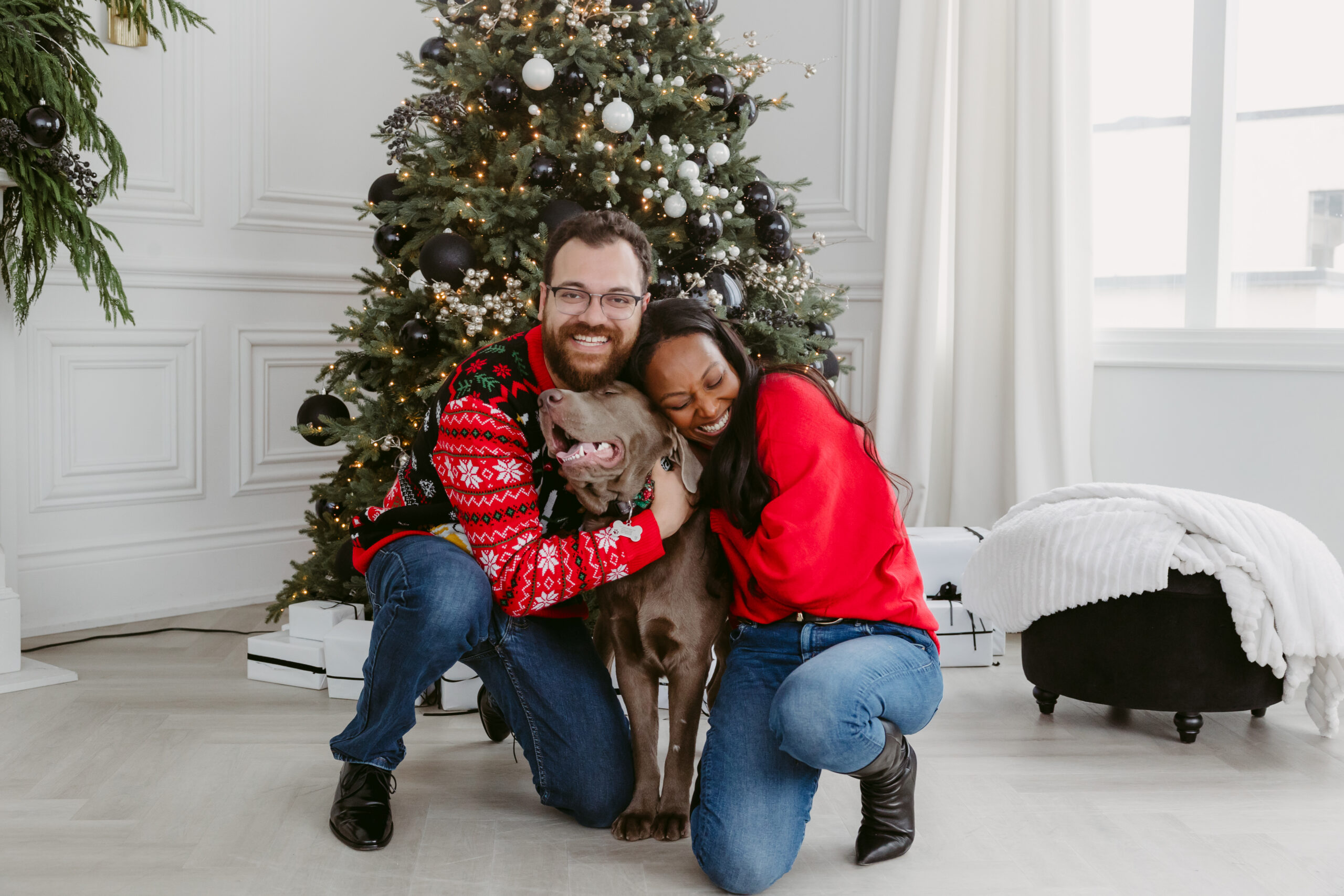 Couple with their dog front of the christmas tree dressed in red.