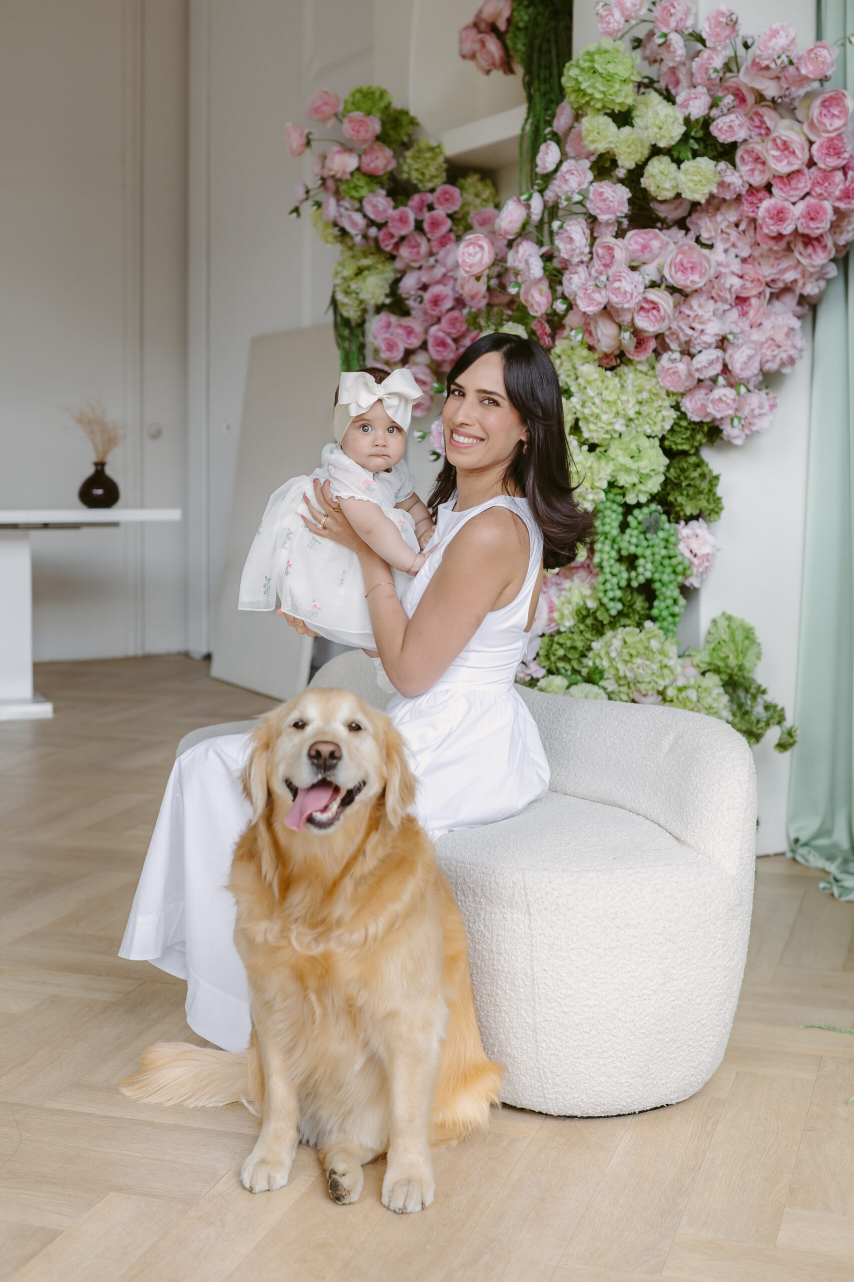Mom in white holding baby girl in white with golden retriever.