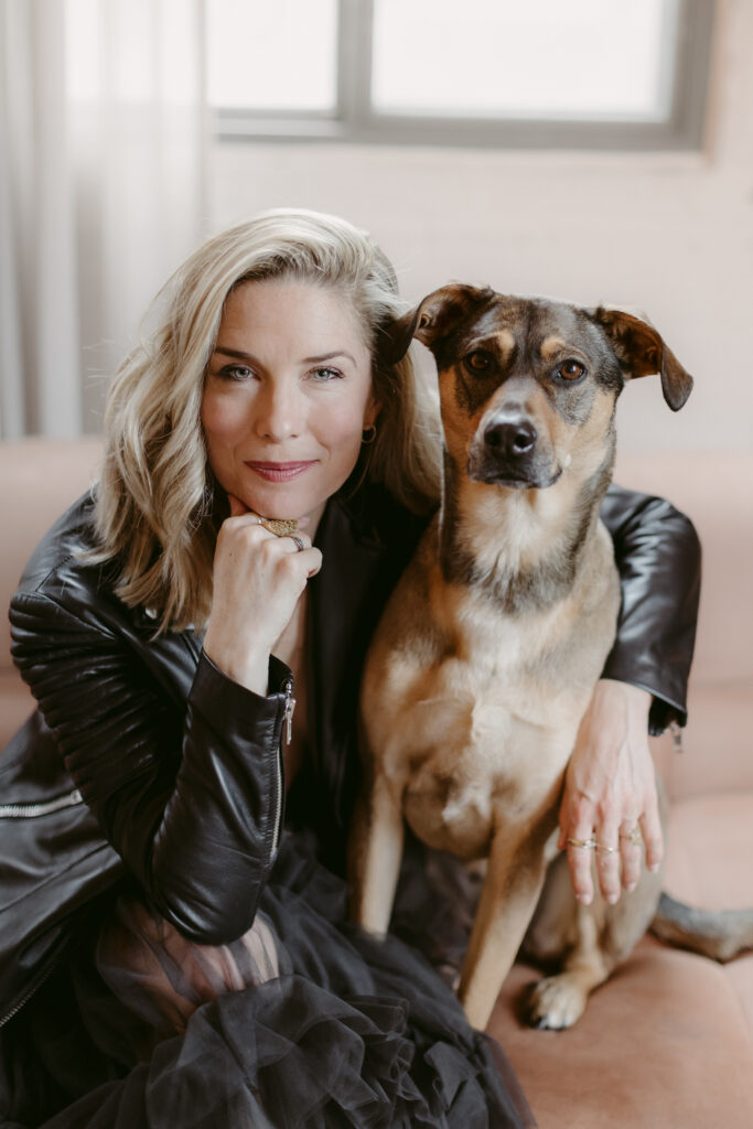 Blonde women in leather hugging her rescue dog, looking at camera.